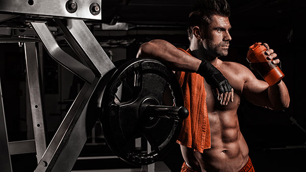 Bodybuilder trinkt angelehnt an einer Trainingsmaschine einen Shake